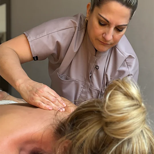 Eine erfahrene Masseurin führt mit ruhiger Konzentration eine gezielte Rückenmassage bei einer entspannt liegenden Kundin in angenehmer Behandlungsatmosphäre durch - Massage & Harmony
